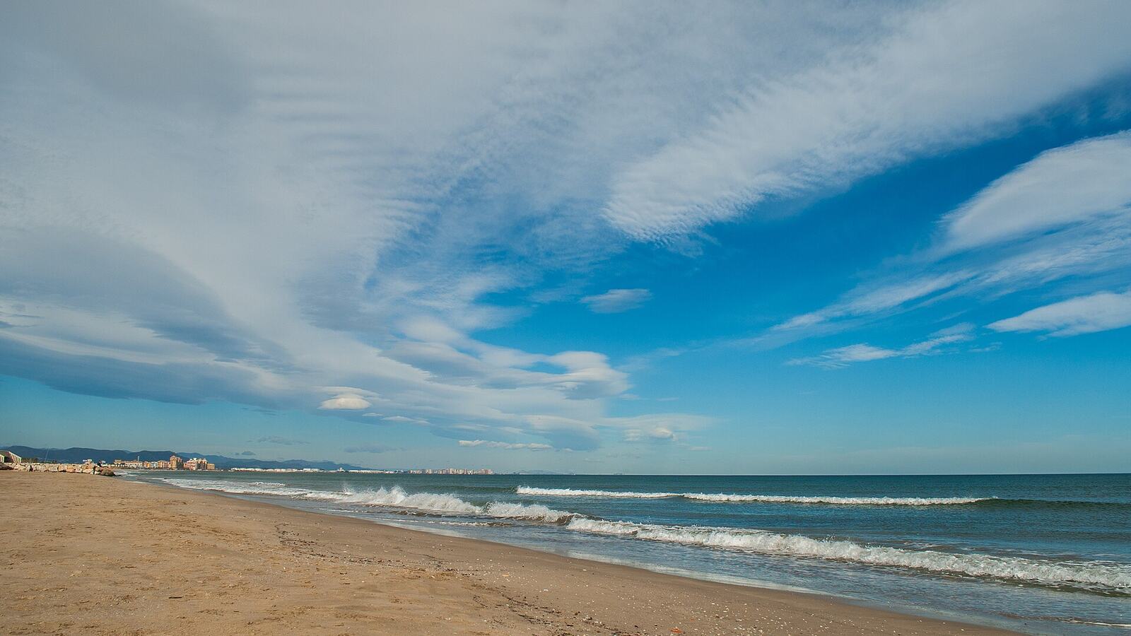 Breed zandstrand aan de Middellandse Zee bij Valencia onder een blauwe lucht met wolken